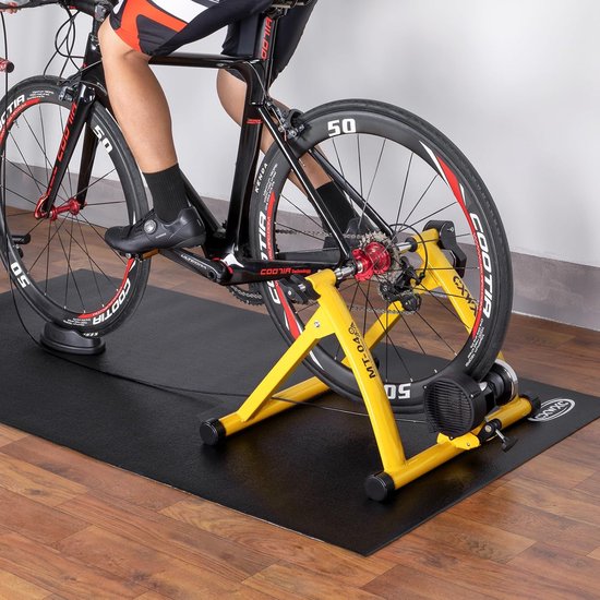 Persoon die op een fiets traint op een gele rollentrainer, op een zwarte mat.