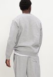 Achterkant van een man in grijze New Balance sweater met wit logo.