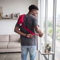 Man met grijs T-shirt knoopt achter zijn rug een rood warmtekussen met linten vast.