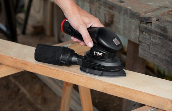 Hand houdt zwarte FERM palm schuurmachine vast op houten plank.