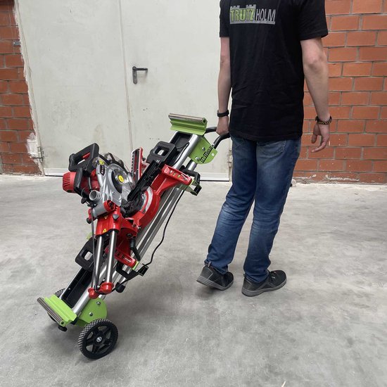 Man met spijkerbroek en zwart T-shirt duwt een groen en rood opgevouwen machineonderstel met zaag, voorzien van wielen.
