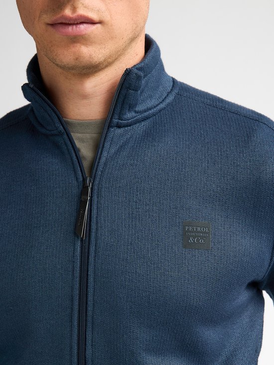 Blauw vest met rits en opgestikte patch met "PETROL INDUSTRIES & CO." tekst op de linkerborst.
