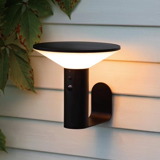 Zwarte wandlamp met sensor op een houten schutting, verlichte tuin met moderne meubels.