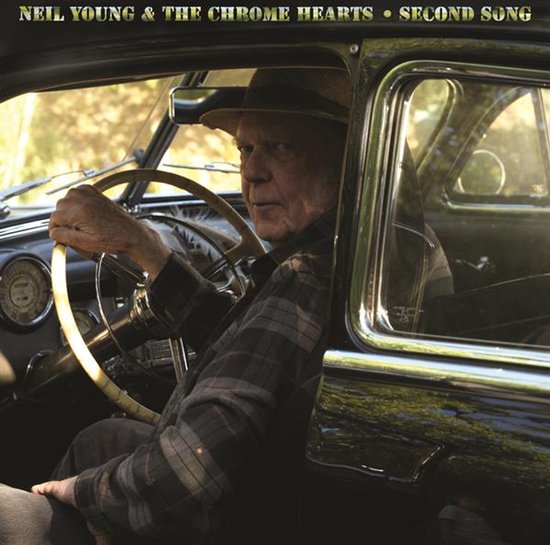 Neil Young met hoed en geruite blouse achter het stuur van een oldtimer.