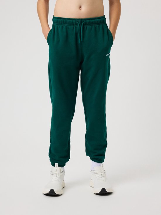 Jongens in een donkergroene joggingbroek met trekkoord en witte sneakers. De broek heeft steekzakken.