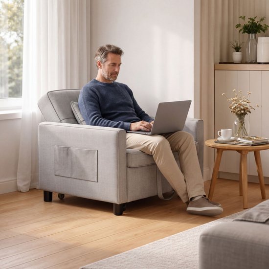 Grijze fauteuil met opbergvakken aan de zijkant, waarin een man zit met een laptop.