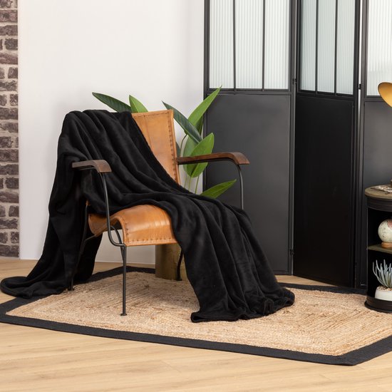 Plaid noir en polaire de 180 x 230 cm, drapé sur un fauteuil en cuir brun.