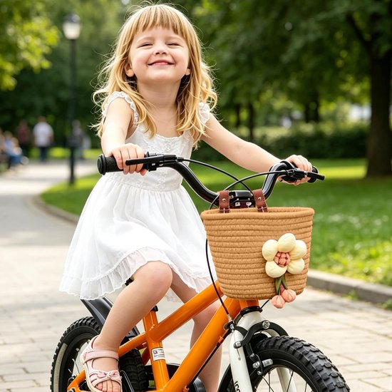 Blond meisje in een witte jurk op een oranje kinderfiets met een beige katoenen mandje met bloemversiering.