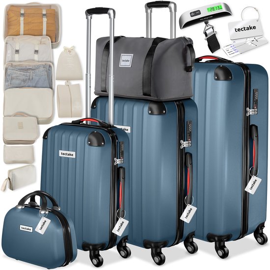 Complete set blauwe koffers, beautycase, reistas, packing cubes, en bagageweegschaal op een witte achtergrond.