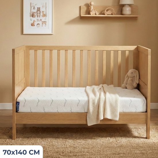 Een houten ledikant met een matras, een beige deken en een konijnenknuffel. Het matras heeft een wit met grijs patroon. Afmeting 70x140 cm.