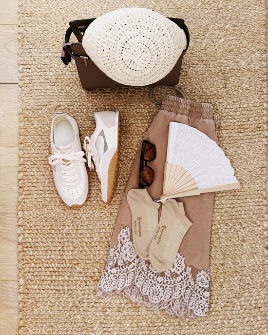Een beige outfit met een witte hoed, zonnebril, witte sneakers en beige Burlington enkelsokken met kant.