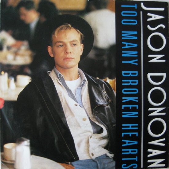 Jason Donovan draagt een zwarte hoed, leren jas en spijkerhemd. De tekst "TOO MANY BROKEN HEARTS JASON DONOVAN" staat verticaal.