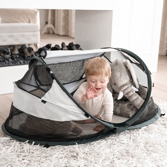 Baby in een grijs-wit Deryan campingbedje met een knuffelolifant.