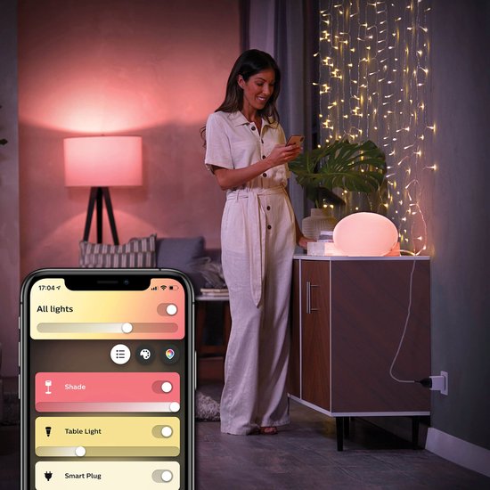 Een vrouw gebruikt een smartphone om de verlichting in een woonkamer te bedienen met een Philips Hue app, inclusief een smart plug.