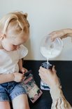 Kind kijkt toe hoe melk uit "mammie" melk bewaarzakje in een babyflesje wordt gegoten.