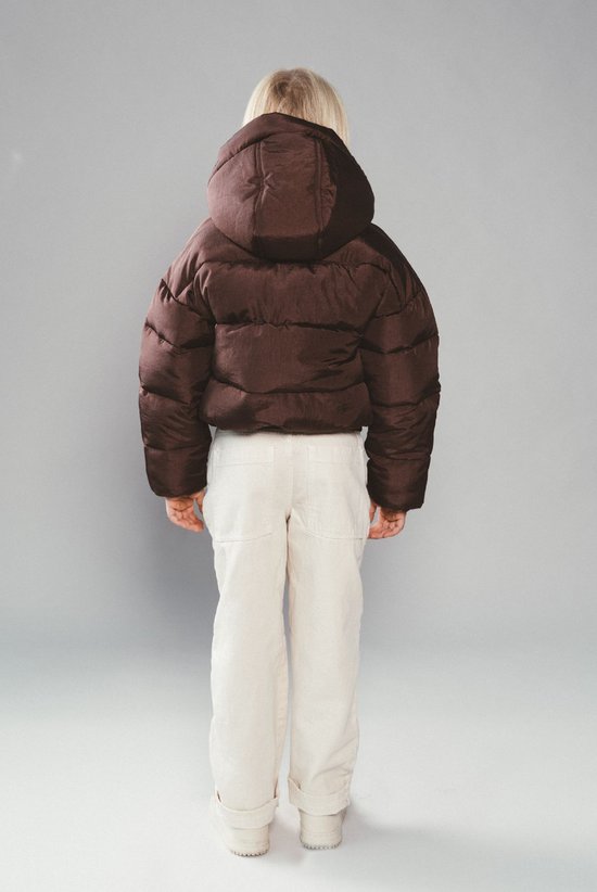 Achterzijde van een kind in een bruine, gewatteerde pufferjas met capuchon en crème kleurige broek.