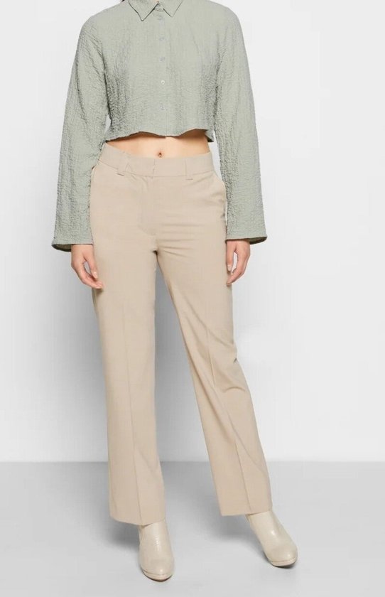 Mannequin portant un pantalon beige taille haute évasé, associé à un haut court vert pâle à manches longues.