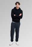 Model met gekruiste armen in donkerblauwe hoodie, bijpassende joggingbroek en witte sneakers.