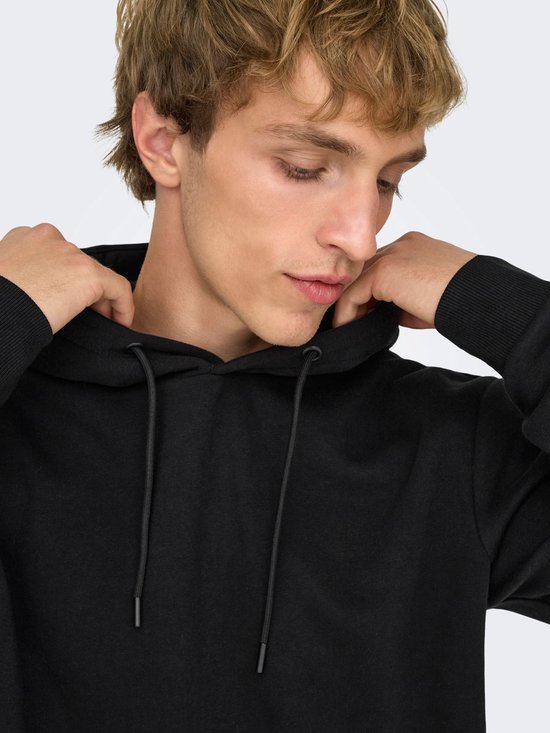Close-up van een man met blonde haren die zijn capuchon en de touwtjes van een zwarte hoodie aanpast.