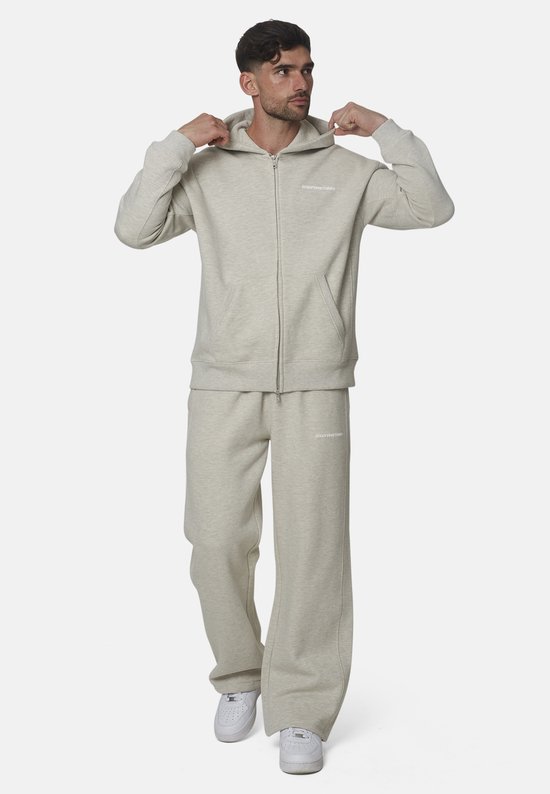 Man met grijze 'GOODFORNOTHING' joggingbroek en hoodie, die de capuchon vastpakt.