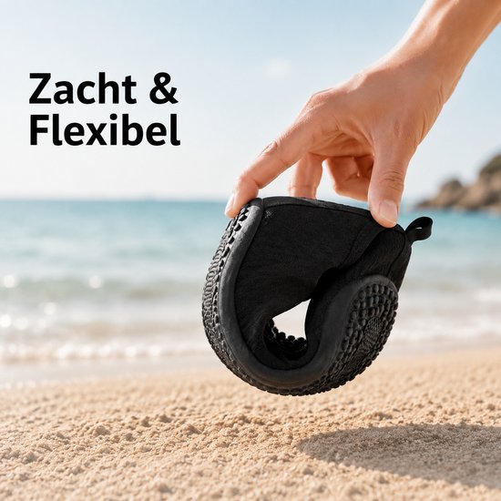 Hand houdt een zwarte, flexibele waterschoen vast op het strand. Beschrijving: Zacht & Flexibel.