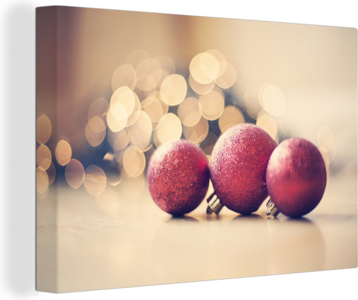 Canvas Schilderij Drie rode kerstballen en kerstverlichting - 150x100 cm - Wanddecoratie