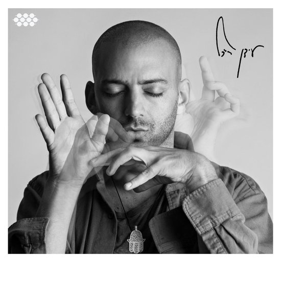 Zwart-wit portret van Idan Raichel met gesloten ogen, handen in gebaren. Hand van Fatima-hanger zichtbaar.