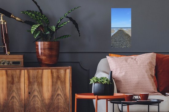 Een poster van een stenen dam aan zee hangt in een woonkamer.