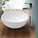 Lavabo rond en blanc en céramique avec un robinet chromé brillant sur un plateau en bois.