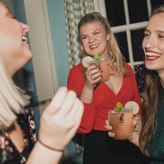 Drie lachende vrouwen houden elk een koperen Moscow Mule beker vast, versierd met limoen en munt.
