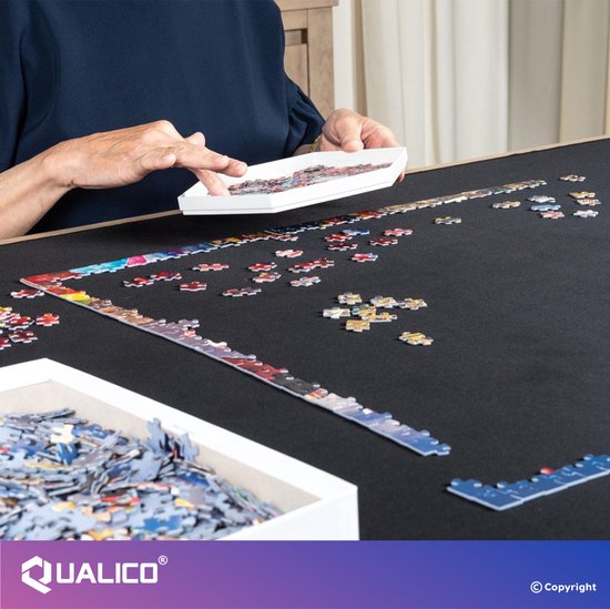 Vrouw puzzelt aan een zwarte mat. De mat toont deels een afgebouwde puzzel.