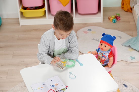 Jongen en BABY born pop bij tafel. Pop draagt blauwe muts en romper met beerprint.