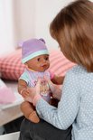Meisje houdt babypop vast. De pop draagt een paarse muts en een paars-geel-roze rompertje.