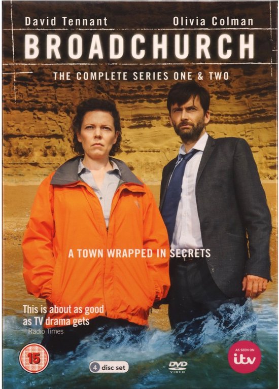 Olivia Colman in oranje jas en David Tennant in grijs pak staan in het water bij een klif.