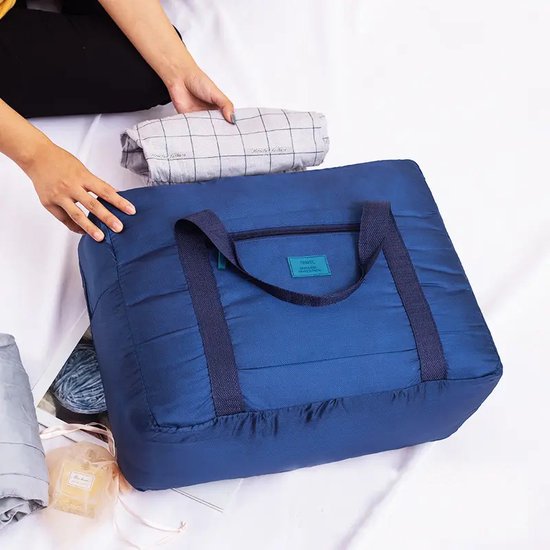 Donkerblauwe, opvouwbare reistas met ritssluiting en hengsels, terwijl er kleding wordt ingepakt.
