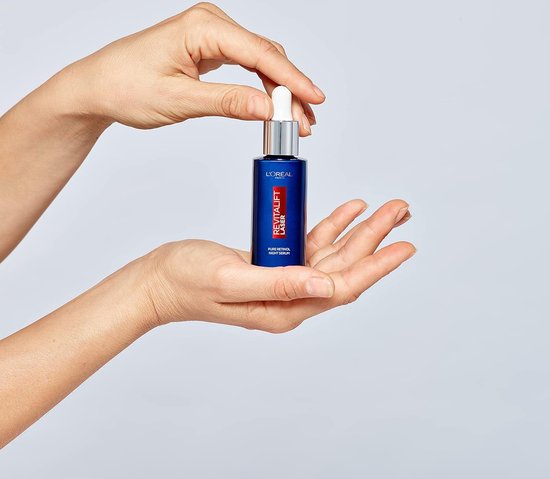 Handen houden een glazen flesje L'Oréal Paris Revitalift Laser Puur Retinol Nacht Serum vast.
