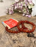 Twee oranje carneool armbanden met rode draden en label op hout