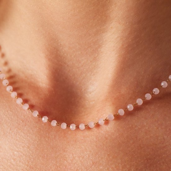 Gouden collier met kleine roze kralen, gedragen op de huid.