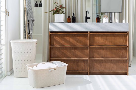 Beige wasmand met deksel en een bijpassende wasmand naast een houten badmeubel.