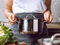 Vrouw met schort houdt RVS pan vast met beide handen