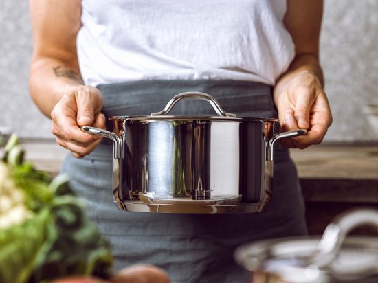 Vrouw met schort houdt RVS pan vast met beide handen