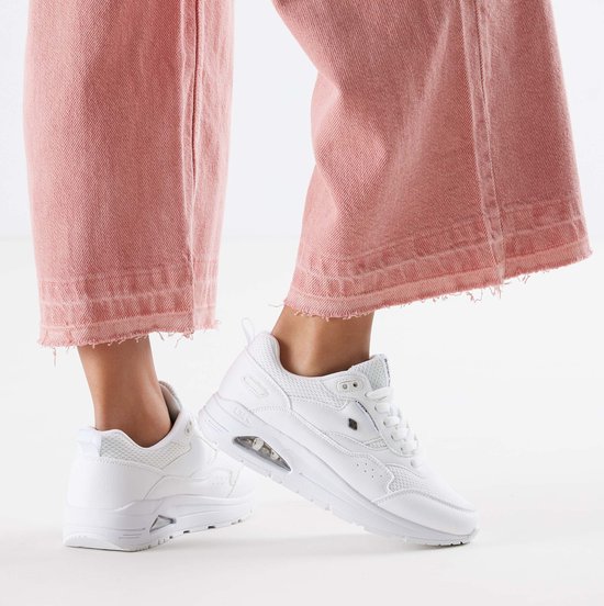 Damesvoeten in roze broek en witte sneakers met mesh en leren details.