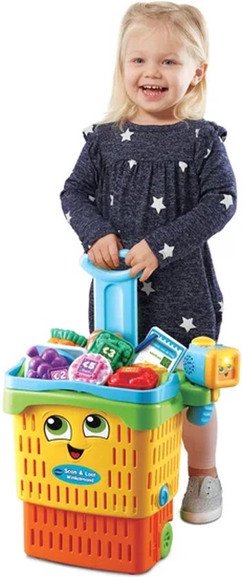 Blond meisje in blauw jurkje met witte sterren, duwt een felgekleurde winkelwagen met speelgoedboodschappen.
