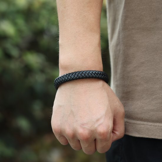 Een close-up van een zwarte gevlochten leren armband om een pols met een zilverkleurige sluiting.
