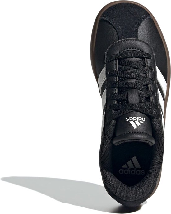 Bovenkant van een zwarte sneaker met witte Adidas-strepen en bruine zool.