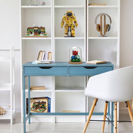 Een blauw bureau met een transparante stolp met bloemen en een model van een tram café op een plank.