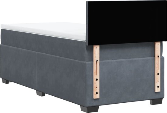 Lit tapissé gris foncé avec matelas blanc et une tête de lit noire montée sur supports en bois.
