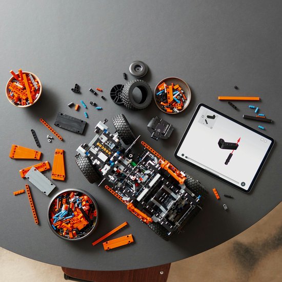 Oranje LEGO Mercedes-Benz G 500 model in aanbouw, met onderdelen en tablet op tafel.