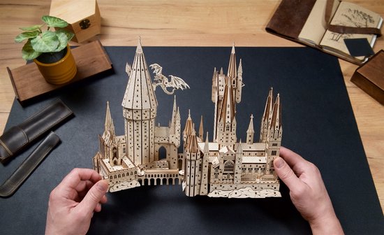 Twee handen houden een houten model van Zweinstein, Harry Potter™.