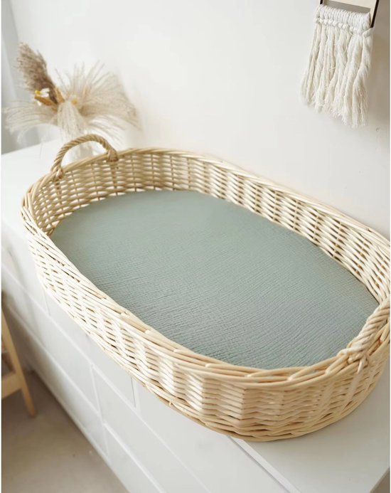 Mintgroen wiegdekje in een rieten wieg, staand op een commode.